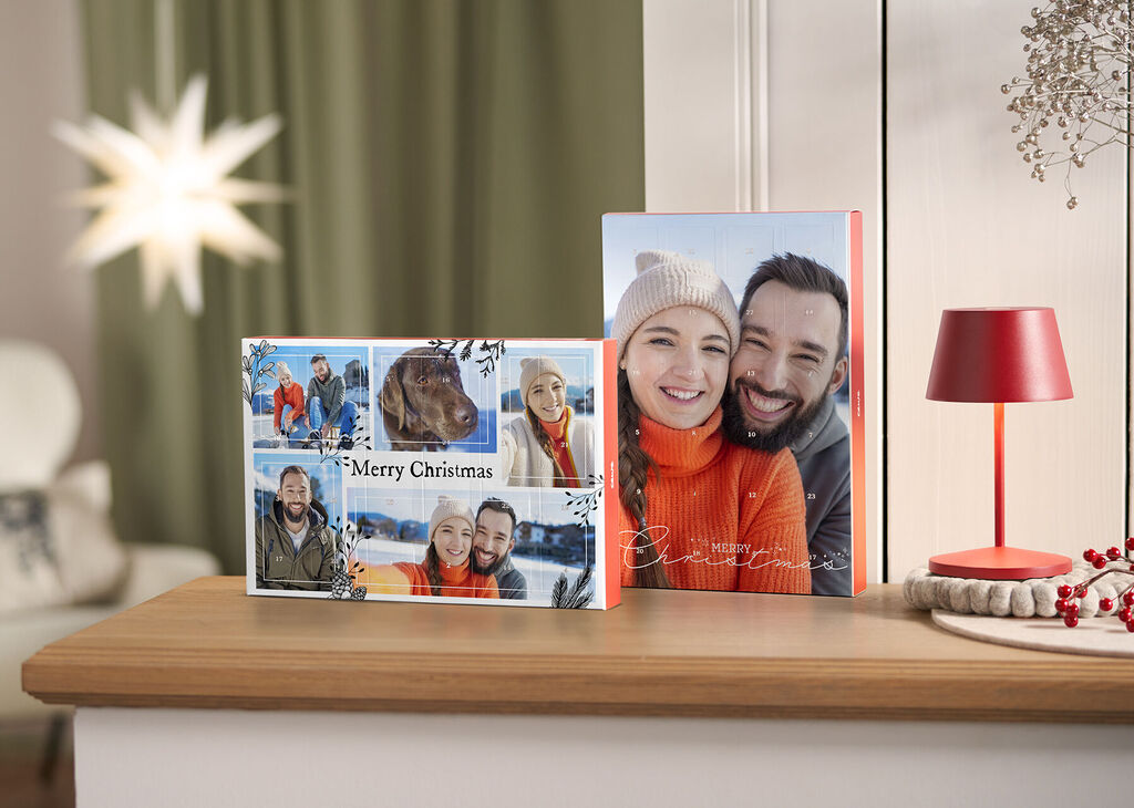 Zwei festlich gestaltete CEWE Fotobücher auf einem Tisch, eines mit einem fröhlichen Weihnachtsmotiv und das andere in warmen Farben.