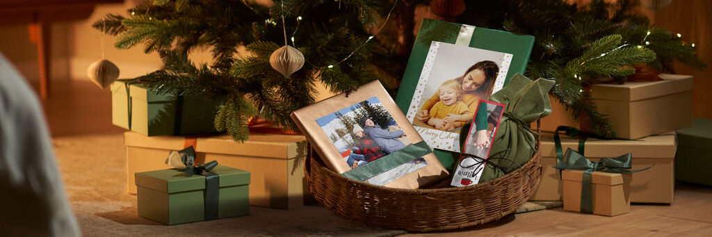 Ein liebevoll gestalteter Geschenkkorb mit einem CEWE Fotobuch, einem Kalender und grünen Geschenken unter einem Weihnachtsbaum