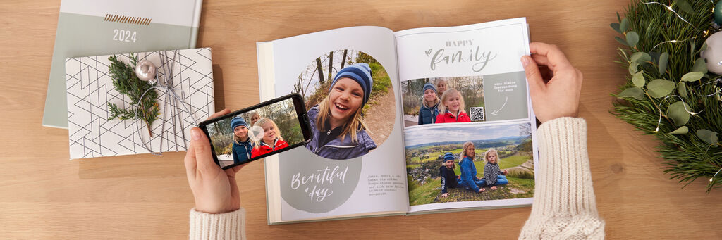 Une personne consulte un livre photo CEWE sur une table tout en tenant un smartphone montrant la même image.