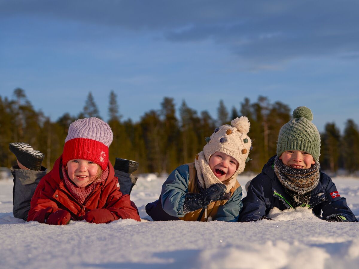 Trois enfants jouent et rient dans la neige avec des bonnets et écharpes d'hiver.