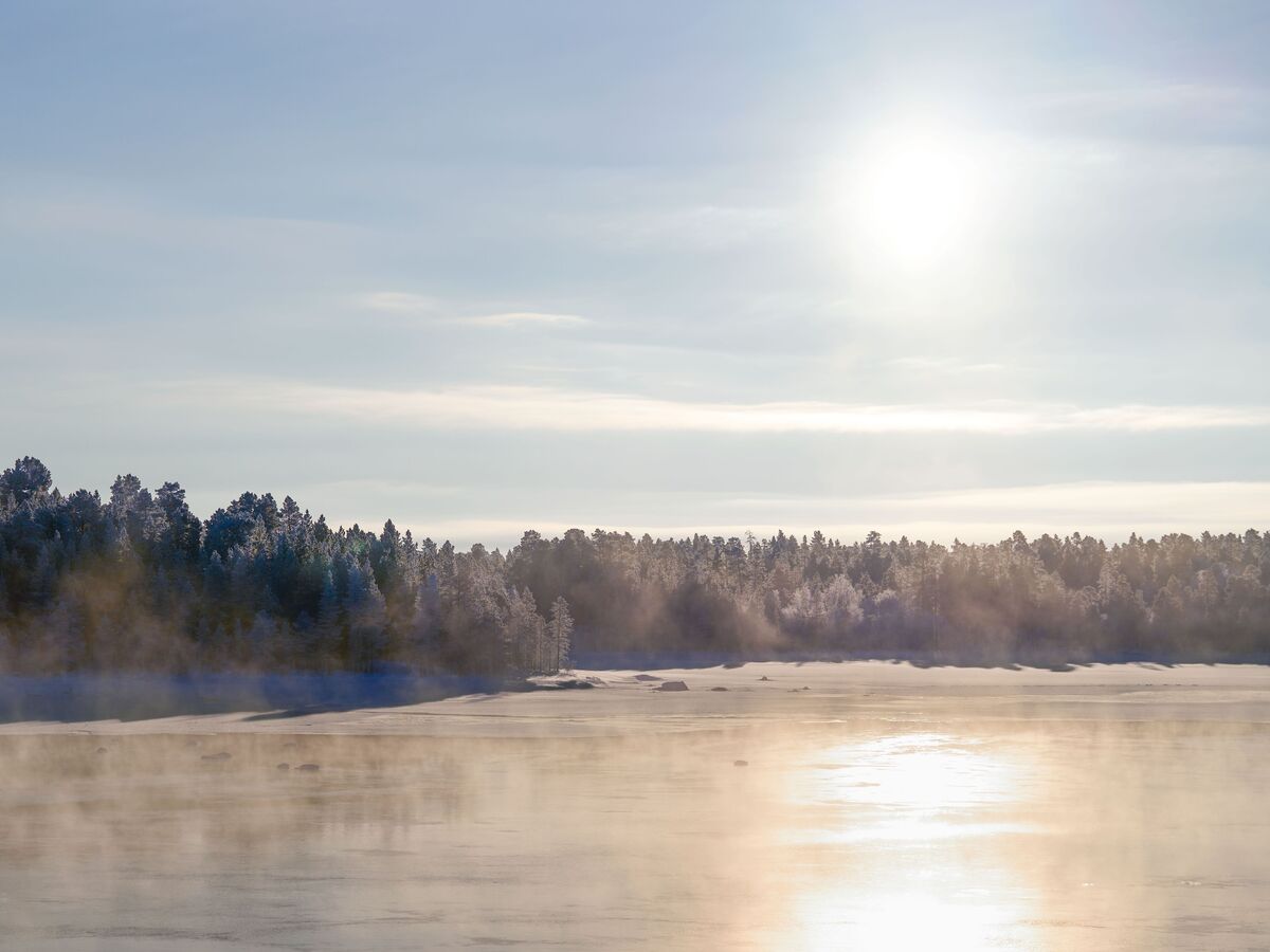 Magnifique paysage d'hiver avec des rayons de soleil au-dessus d'un lac gelé et d'une rive boisée.