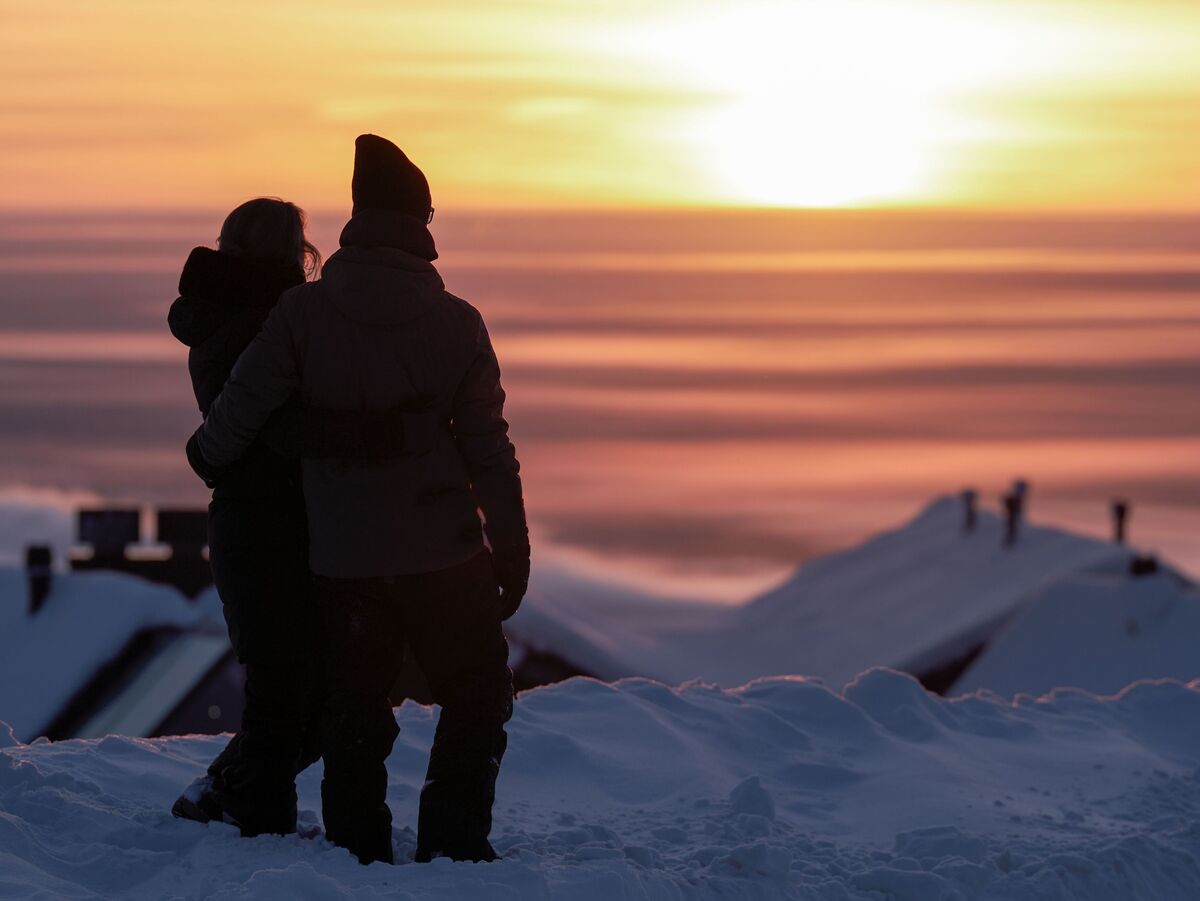 Una coppia si abbraccia nella neve durante un tramonto, con colori caldi nel cielo.