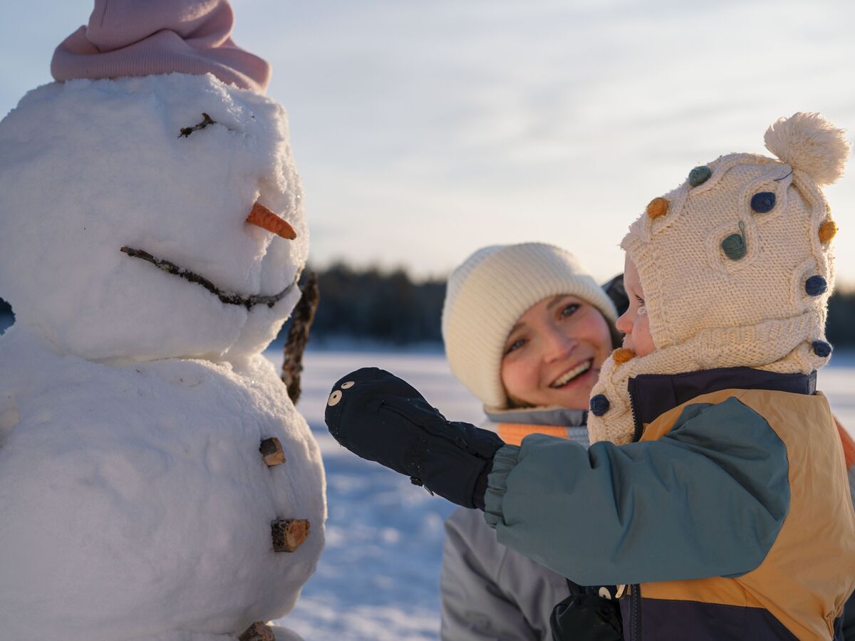 Un bambino felice costruisce un pupazzo di neve in inverno. Ha una carota come naso e un cappello.